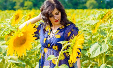 Çekici, genç, esmer, kıvırcık kadın ayçiçeği çayırında, altın bir tarlada güneşli bir günde hayatın tadını çıkar.