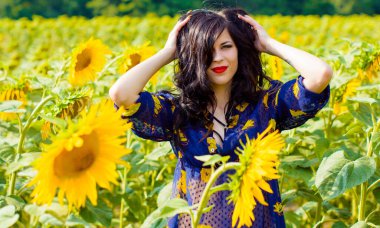 Çekici, genç, esmer, kıvırcık kadın ayçiçeği çayırında, altın bir tarlada güneşli bir günde hayatın tadını çıkar.