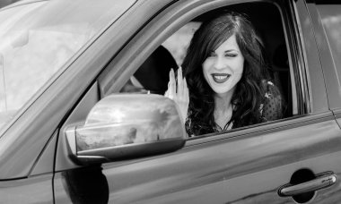 Güzel, kıvırcık esmer kadın bir arabada oturur ve makyajını düzeltir, kadınlar için tehlikelidir.