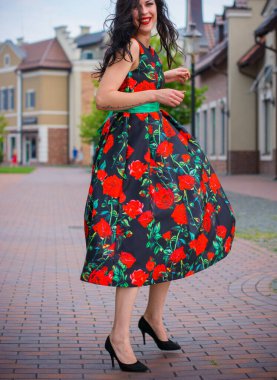 Kıvırcık saçlı, 50 'li yaşlarda, siyah elbiseli, kırmızı güllü muhteşem esmer kadın. Güzel kız sokaklarda yürüyor ve iyi bir ruh hali içinde harika hissediyor.