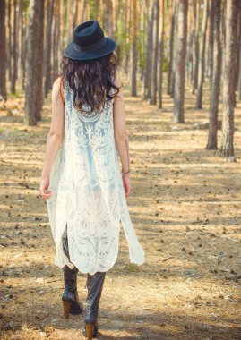 Siyah şapkalı, dantelli, bohem hırkalı, güzel, kıvırcık esmer kadın. Ormanda yürüyor ve ahşap yakındaki hayatı düşünüyor.