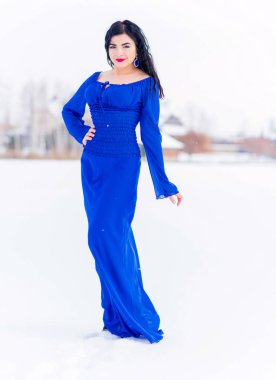 Kar tarlasında mavi elbiseli seksi bir kadın, şehvetli bir konsept. Kış zamanı şık bir kadın portresi.