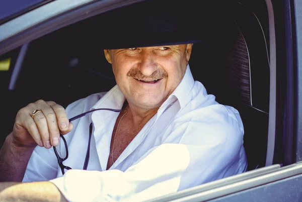 Mature stylish European or American man wear black hat, glasses and white shirt driven car, modern and hipster style for older people. Such a good mood at pretty day