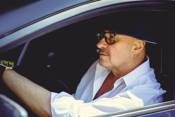 Mature stylish European or American man wear black hat, glasses and white shirt driven car, modern and hipster style for older people. Such a good mood at pretty day