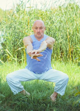 Kıdemli adam doğa üzerinde egzersiz yapar. Fizyoterapi konsepti. Sokakta spor yapan yaşlı bir adam. Sazlıklara karşı egzersiz yaparken kaslarını esneten olgun bir adam..