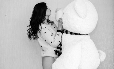 Genç ve güzel bir kadın, büyük oyuncak ayıya sarılıyor. Mutlu bir şekilde gülümsüyor. Komik kız ve büyük oyuncak ayı. Sevgililer günü hediyeleri