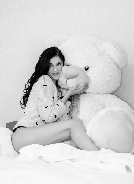 Young beautiful woman hug big teddy bear soft toy happy smiling at morning in bedroom. Funny girl and big toy bear. Valentine day gifts