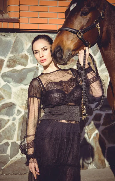 乗馬のエレガントな女性は彼女の馬に話している 帽子の女性と乗馬の肖像画 背景にライダーと古い安定した馬 — ストック写真