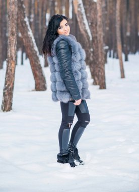 Gri kürklü kadın kış günü ormanda yürür, bayanlar gündelik moda.