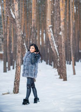 Gri kürklü kadın kış günü ormanda yürür, bayanlar gündelik moda.