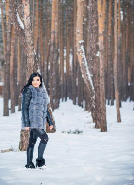 Gri kürklü kadın kış günü ormanda yürür, bayanlar gündelik moda.