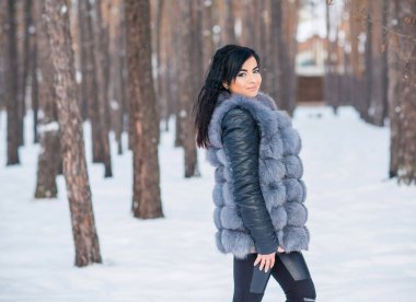 Gri kürklü kadın kış günü ormanda yürür, bayanlar gündelik moda.