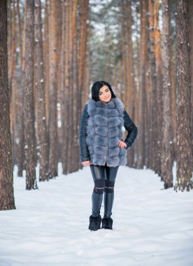 Gri kürklü kadın kış günü ormanda yürür, bayanlar gündelik moda.