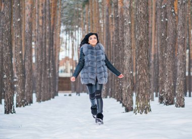 Gri kürklü kadın kış günü ormanda yürür, bayanlar gündelik moda.