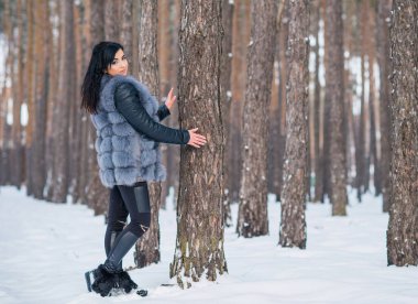 Gri kürklü kadın kış günü ormanda yürür, bayanlar gündelik moda.