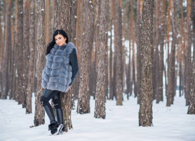 Gri kürklü kadın kış günü ormanda yürür, bayanlar gündelik moda.