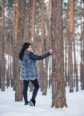 Gri kürklü kadın kış günü ormanda yürür, bayanlar gündelik moda.