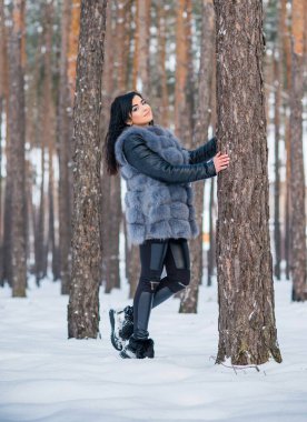 Gri kürklü kadın kış günü ormanda yürür, bayanlar gündelik moda.