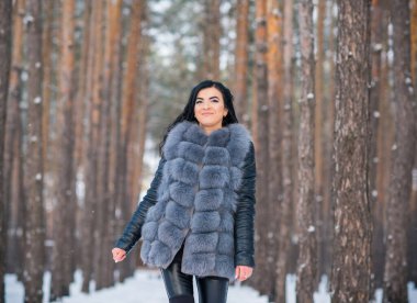Gri kürklü kadın kış günü ormanda yürür, bayanlar gündelik moda.