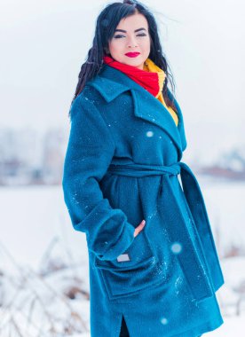Kış tatili konsepti. Tarz sahibi Arap kadın dışarıda karlı bir güne bakıyor. Mavi alpaka paltolu kadın ve kış günü açık havada kırmızı-sarı atkı.
