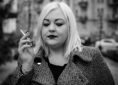 Açık havada sigara içen iri yarı, Avrupalı bir kız. Kadınlar arasında sigara içme sorunları. Sigara içmenin ağırlık ve şekle etkisi