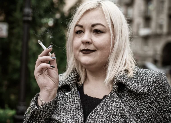 Açık havada sigara içen iri yarı, Avrupalı bir kız. Kadınlar arasında sigara içme sorunları. Sigara içmenin ağırlık ve şekle etkisi