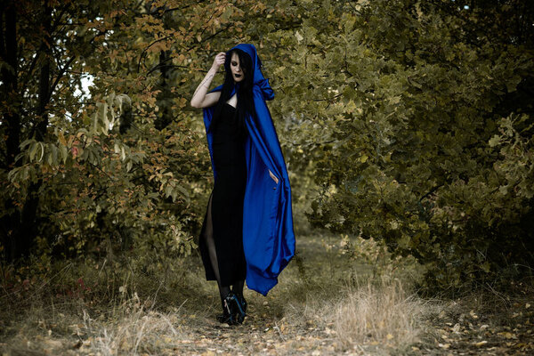 Halloween time, witchcraft, modern gothic girl in blue cloak celebrate. Good ideas for photoshoots, cosplay
