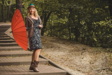 Sonbaharda modaya uygun giyinen, moda konsepti olan orta yaşlı bir kadınla parkta sahne alan bir kadın.