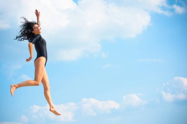 Tayt giymiş genç bir kadın kumda, trenlerde jimnastik yapıyor ve iyi davranıyor. Eğitimin zevki. Kum tepelerinde bir kız ince bir figür sergiliyor