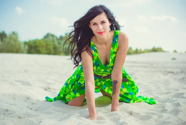 Çölde kumların üzerinde yeşil bir yaz elbisesi içinde desenleri olan güzel bir kadın. Şık bir görünüş için parlak elbiseler ve tarz..