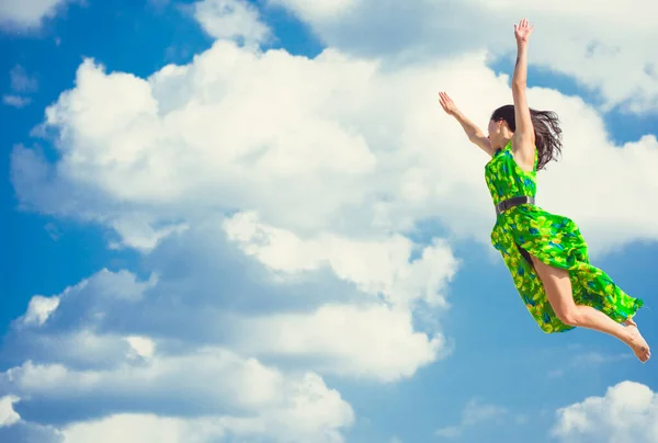 A woman on a bright green dress flies and hovers in the sky. The girl in the jump feels from prejudice. Beauty and dynamics in flight. The concept of faith in oneself and freedom