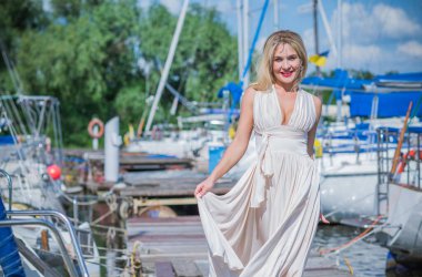 Yat kulübündeki güzel sarışın bayan. Açık havada uçan ipek beyaz elbiseli kadın, dinlenme zamanı.