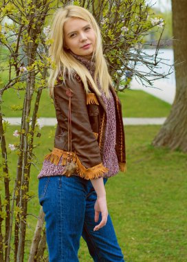 Doğada genç ve seksi sarışın kız ve nehir kenarında sazlıklar ve Amerikan kırsalında ağaçlar deri ceketli, mavi kazaklı, güzel yüzlü ve güzel gözlü kahverengi çizmeli.