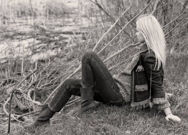 Doğada genç ve seksi sarışın kız ve nehir kenarında sazlıklar ve Amerikan kırsalında ağaçlar deri ceketli, mavi kazaklı, güzel yüzlü ve güzel gözlü kahverengi çizmeli.
