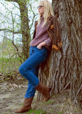 Doğada genç ve seksi sarışın kız ve nehir kenarında sazlıklar ve Amerikan kırsalında ağaçlar deri ceketli, mavi kazaklı, güzel yüzlü ve güzel gözlü kahverengi çizmeli.