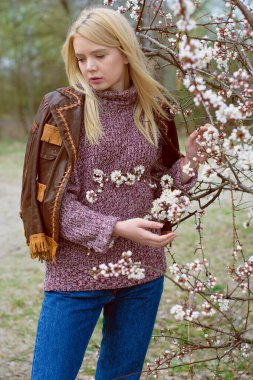 Doğada genç ve seksi sarışın kız ve nehir kenarında sazlıklar ve Amerikan kırsalında ağaçlar deri ceketli, mavi kazaklı, güzel yüzlü ve güzel gözlü kahverengi çizmeli.