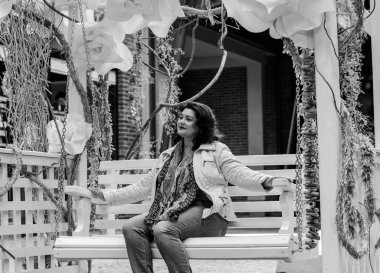 Yetişkin, iri yapılı, Amerikan ya da Avrupa görünümlü basit bir kadın şehirde hayatın tadını çıkarıyor. Fazla kilolu, ceketli ve fularlı hoş bir bayan şehrin eski bir köşesinde dolaşıyor.