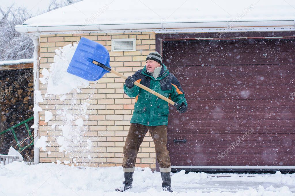 Winter, people and problem concept - closeup of man digging snow with shovel near yard. Man standing with blue shovel and he snow cleaning. Winter routine concept.