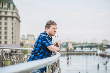 Ciddi ruh hali olan genç adam şehir manzarasına bak, tombul insanlar konsepti, büyük şehir hayatı. Şehir merkezindeki adamın resmi