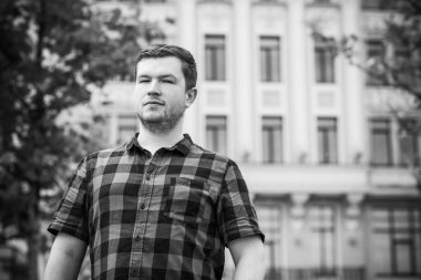 Ciddi ruh hali olan genç adam şehir manzarasına bak, tombul insanlar konsepti, büyük şehir hayatı. Şehir merkezindeki adamın resmi