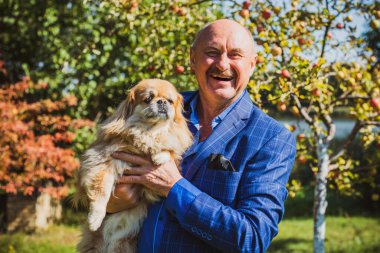 Emekli olmuş yaşlı bir adam, parkta gezintiye çıkmış kırmızı Pekin hayvanıyla köpek sever. Hayvanların sevgisini ve bakımını kavrayın. İyi insanlar evcil hayvanlara bakar.