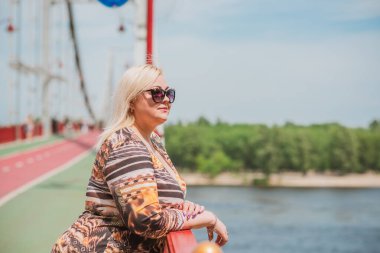 Büyük beden, Amerikan ya da Avrupalı görünümlü bir kadın şehirde hayatın tadını çıkarıyor. Aşırı kilolu genç bir bayan, şehrin merkezinde şık bir şekilde giyinmiş. Doğal güzellik.