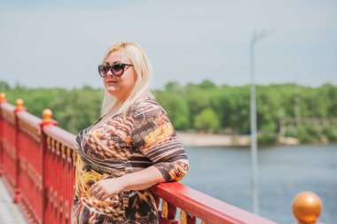 Büyük beden, Amerikan ya da Avrupalı görünümlü bir kadın şehirde hayatın tadını çıkarıyor. Aşırı kilolu genç bir bayan, şehrin merkezinde şık bir şekilde giyinmiş. Doğal güzellik.