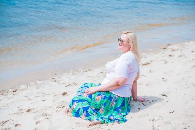 Artı plajda bir model. Şişman kadın hayattan zevk alıyor. Nehir kenarındaki doğada, kumların üzerinde dinlenen güzel bir kadın. Kadın hayatı kavramı.