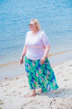 Artı plajda bir model. Şişman kadın hayattan zevk alıyor. Nehir kenarındaki doğada, kumların üzerinde dinlenen güzel bir kadın. Kadın hayatı kavramı.