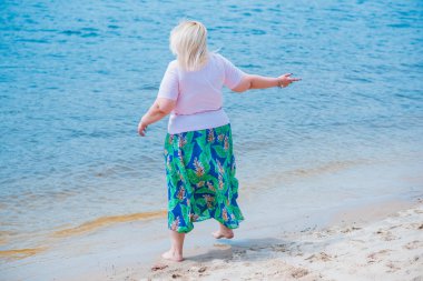 Artı plajda bir model. Şişman kadın hayattan zevk alıyor. Nehir kenarındaki doğada, kumların üzerinde dinlenen güzel bir kadın. Kadın hayatı kavramı.