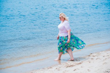 Artı plajda bir model. Şişman kadın hayattan zevk alıyor. Nehir kenarındaki doğada, kumların üzerinde dinlenen güzel bir kadın. Kadın hayatı kavramı.