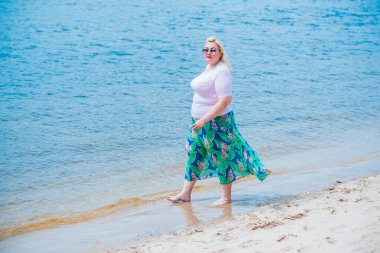 Artı plajda bir model. Şişman kadın hayattan zevk alıyor. Nehir kenarındaki doğada, kumların üzerinde dinlenen güzel bir kadın. Kadın hayatı kavramı.