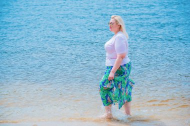 Artı plajda bir model. Şişman kadın hayattan zevk alıyor. Nehir kenarındaki doğada, kumların üzerinde dinlenen güzel bir kadın. Kadın hayatı kavramı.