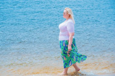 Artı plajda bir model. Şişman kadın hayattan zevk alıyor. Nehir kenarındaki doğada, kumların üzerinde dinlenen güzel bir kadın. Kadın hayatı kavramı.